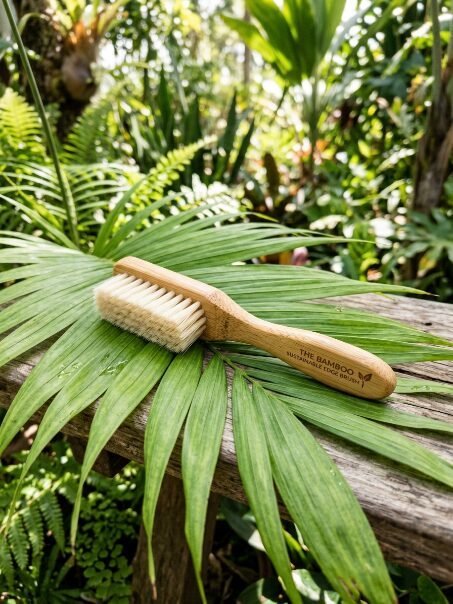 Close-up of a sustainable bamboo edge brush placed on a large leaf outdoors.