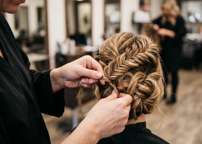 Close up of a stylist hands pinning a messy blonde fishtail braid into an updo style.