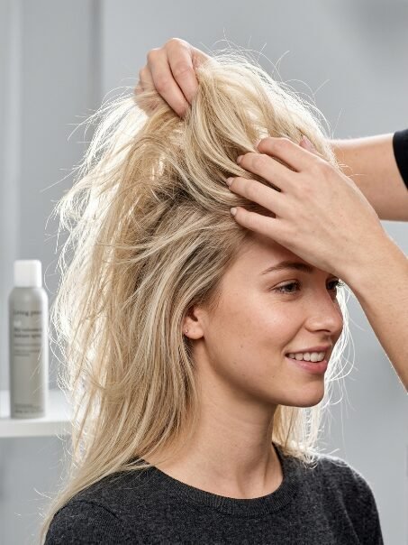 Professional stylist using hands to add texture and volume to a woman's long blonde hair.