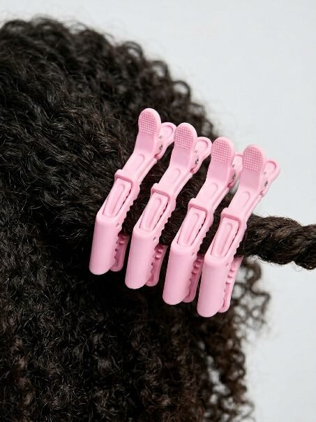 Close up of four light pink plastic hair clips gripping strands of textured black curly hair.