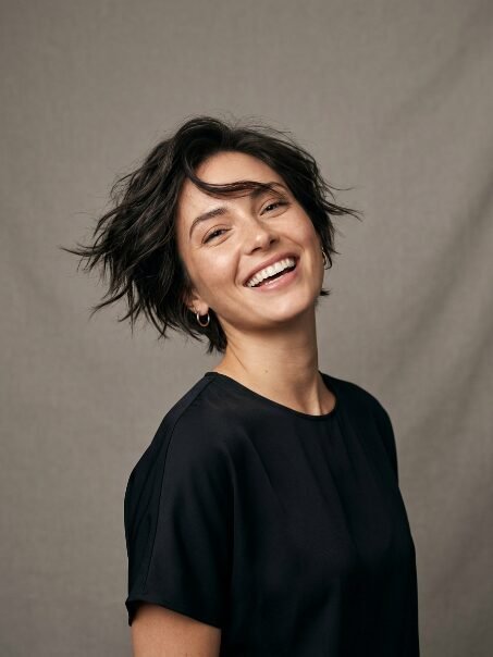 Portrait of a cheerful young woman wearing a black top against a grey background.