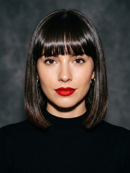 Close-up portrait of a woman wearing a black turtleneck with a chin-length bob hairstyle and bold red lipstick.