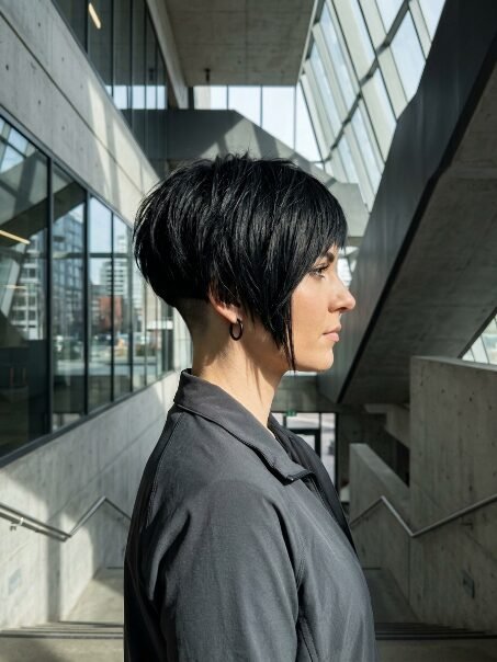 Side profile of a woman with a dark short hair style featuring an undercut and long swept bangs.