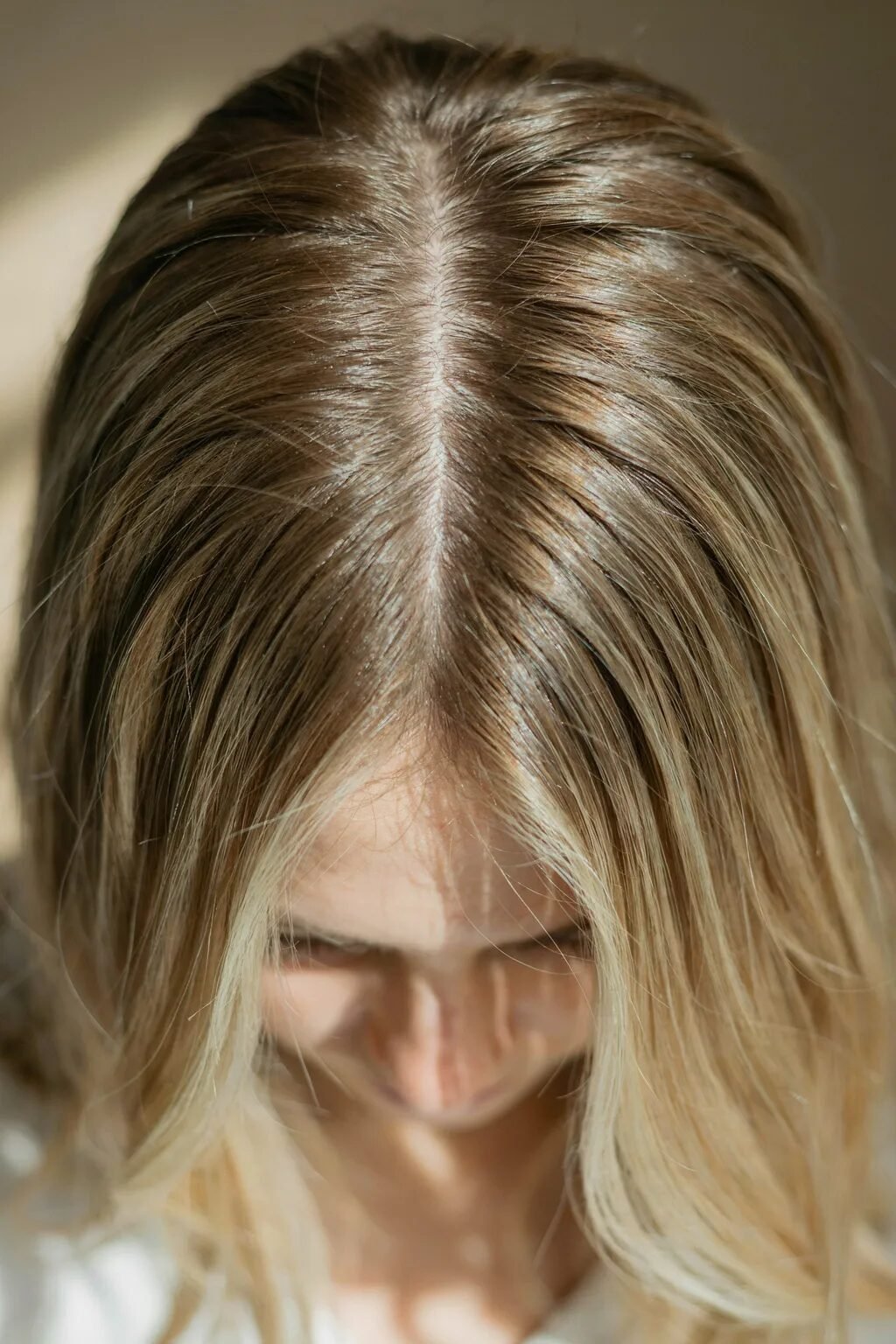 Top-down view of a woman's scalp showing blonde hair with highlights and a clean middle part