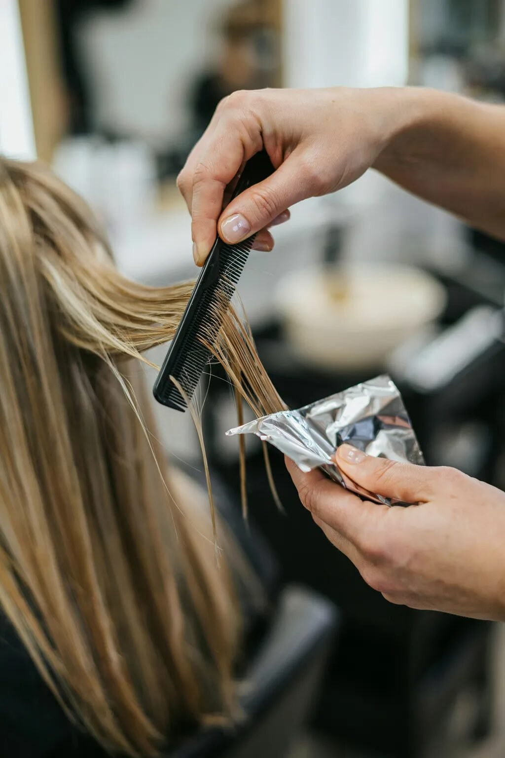 Close up of a salon professional holding a black comb and silver foil while treating client hair.