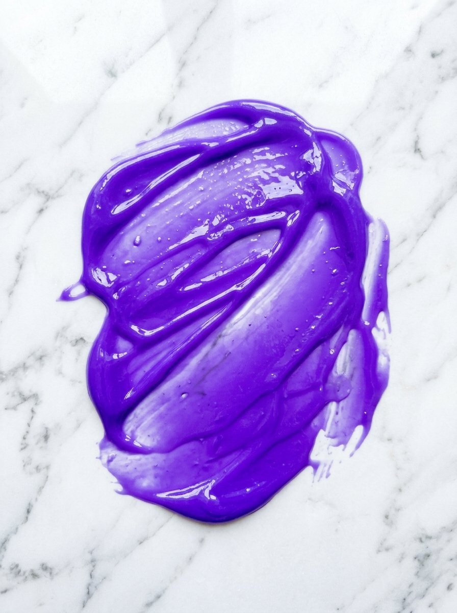 A thick, glossy purple paste spread across a smooth white and grey veined marble surface.